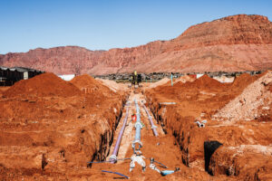 Underground utility trench with installed water/sewer lines and red rock backdrop in St. George, Utah.